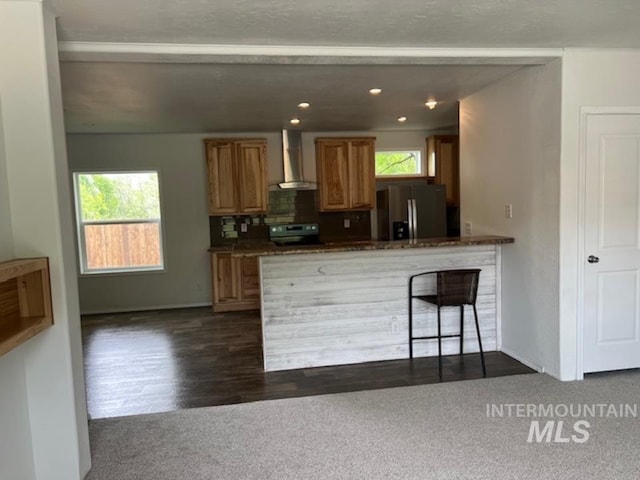 kitchen featuring stainless steel fridge with ice dispenser, wall chimney range hood, electric range, dark colored carpet, and a peninsula