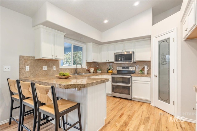 kitchen featuring appliances with stainless steel finishes, a kitchen bar, kitchen peninsula, and white cabinets