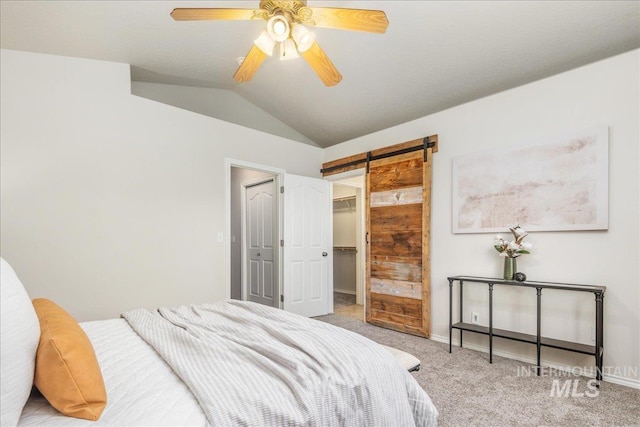 bedroom featuring vaulted ceiling, a walk in closet, light colored carpet, ceiling fan, and a barn door