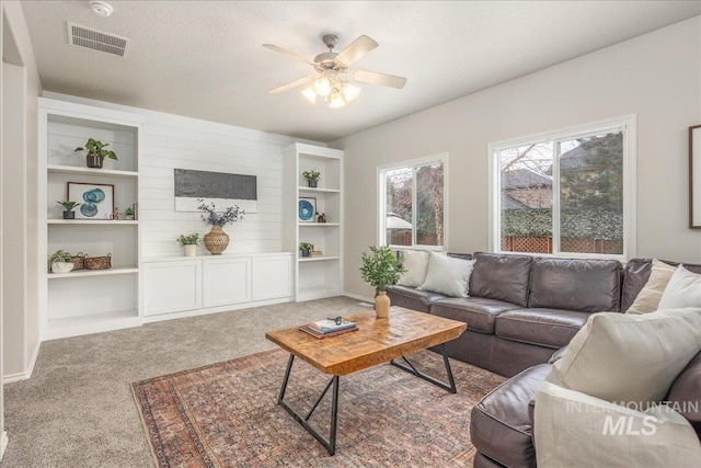 carpeted living room with ceiling fan, built in shelves, and a textured ceiling