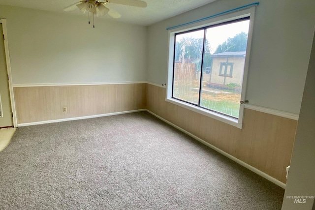 empty room featuring carpet flooring, ceiling fan, and wood walls