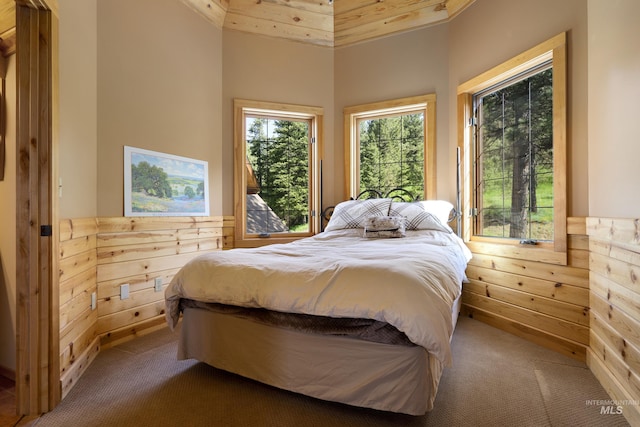 carpeted bedroom featuring high vaulted ceiling and wood walls