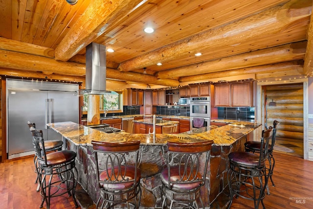 kitchen with appliances with stainless steel finishes, island exhaust hood, log walls, and beamed ceiling