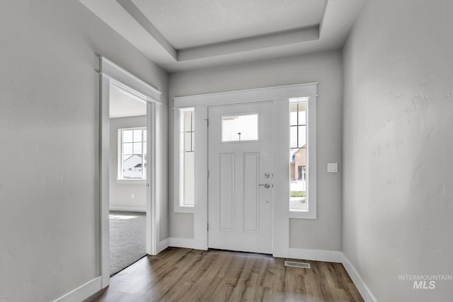 entryway featuring a tray ceiling, light hardwood / wood-style floors, and a textured ceiling