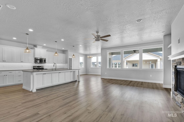 unfurnished living room featuring light hardwood / wood-style flooring, sink, a stone fireplace, ceiling fan, and a textured ceiling