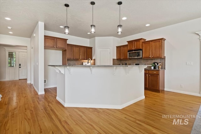 5315 N Red Hills Pl, Meridian, ID 83646 - kitchen with stainless steel microwave, brown cabinets, light wood-type flooring, tasteful backsplash, and a breakfast bar
