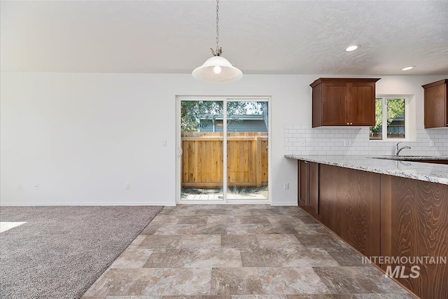 kitchen featuring pendant lighting, sink, decorative backsplash, light stone counters, and a textured ceiling