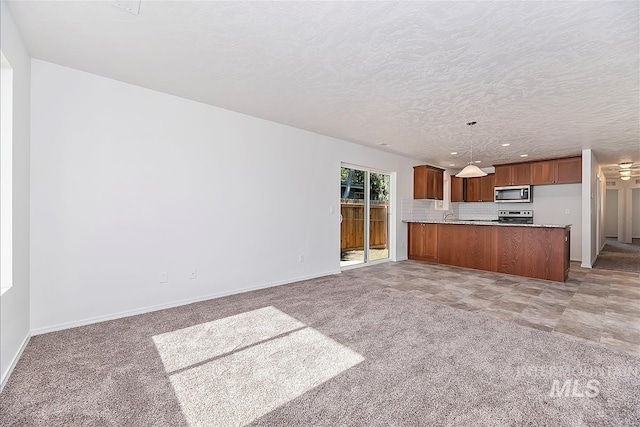 kitchen with appliances with stainless steel finishes, pendant lighting, tasteful backsplash, light colored carpet, and kitchen peninsula