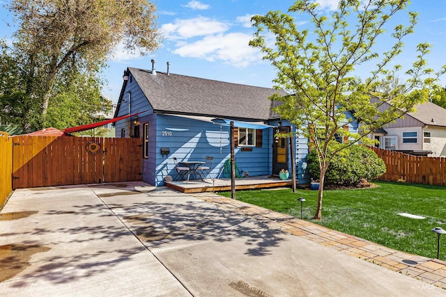 exterior space with a front yard, roof with shingles, a deck, a gate, and fence