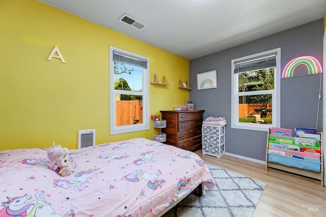 bedroom featuring baseboards, visible vents, multiple windows, and wood finished floors