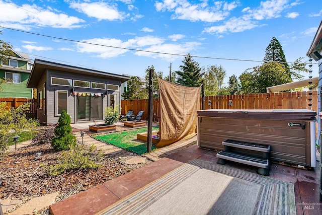 view of patio / terrace with a hot tub, an outbuilding, a garden, and a fenced backyard