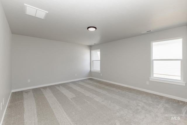 spare room featuring light colored carpet, visible vents, and baseboards