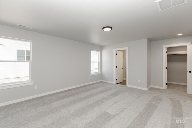 unfurnished bedroom featuring light colored carpet, a walk in closet, visible vents, and baseboards