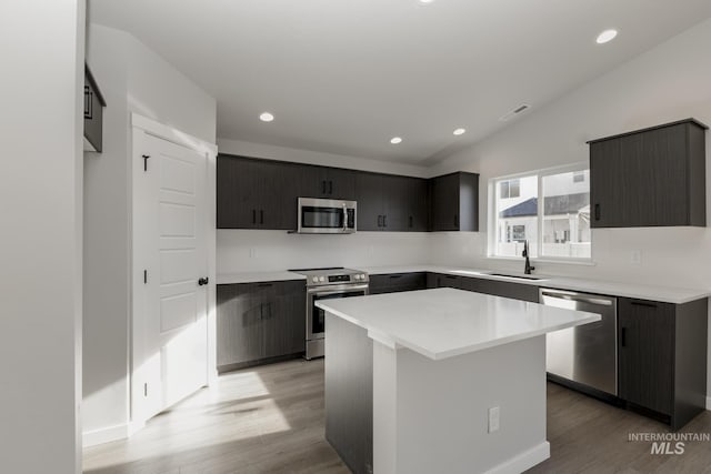 kitchen with sink, stainless steel appliances, a kitchen island, vaulted ceiling, and light wood-type flooring