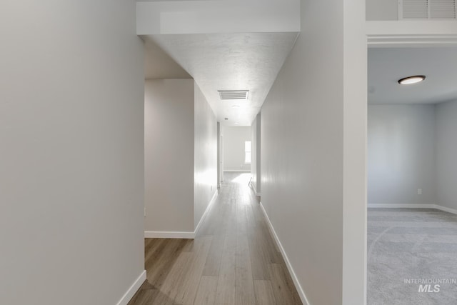 hall featuring wood finished floors, visible vents, and baseboards