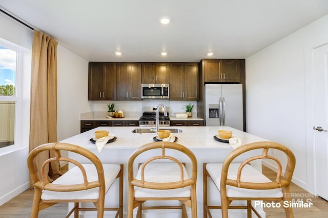 kitchen with dark brown cabinetry, sink, stainless steel appliances, and a center island with sink