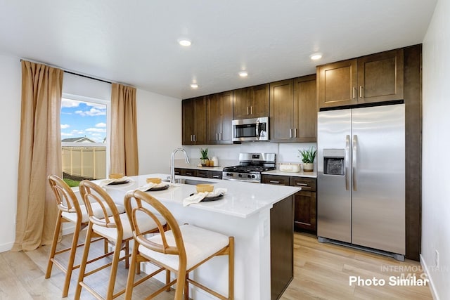 kitchen with a breakfast bar, dark brown cabinets, a center island with sink, light hardwood / wood-style flooring, and appliances with stainless steel finishes