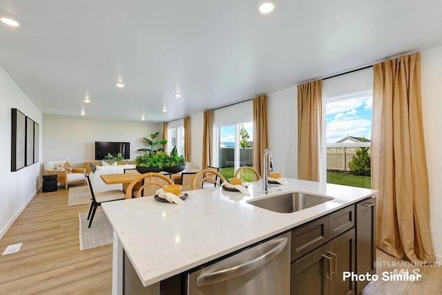 kitchen featuring sink, light stone counters, a kitchen island with sink, dishwasher, and light hardwood / wood-style floors