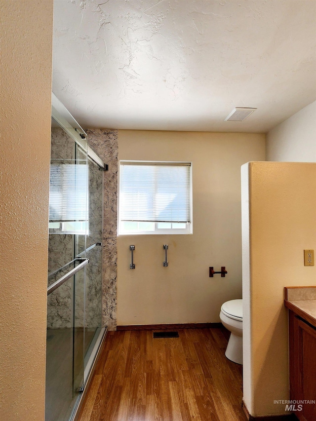 bathroom featuring wood-type flooring, a shower with shower door, vanity, and toilet