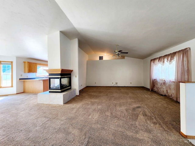 unfurnished living room featuring a tile fireplace, lofted ceiling, ceiling fan, and light colored carpet