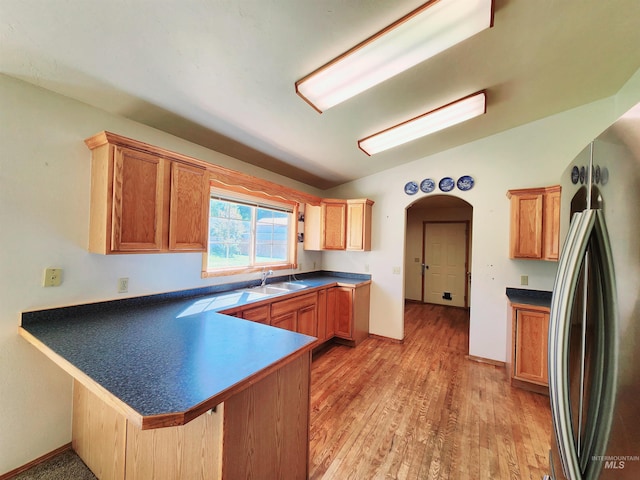 kitchen with sink, lofted ceiling, kitchen peninsula, light hardwood / wood-style flooring, and stainless steel fridge