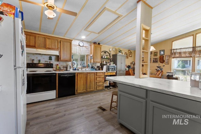 kitchen with freestanding refrigerator, light wood-type flooring, black dishwasher, under cabinet range hood, and range with electric stovetop
