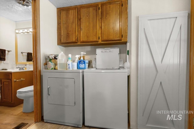washroom with light wood-style flooring, visible vents, a textured ceiling, cabinet space, and washer and clothes dryer