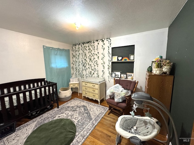 bedroom with hardwood / wood-style flooring, a nursery area, and a textured ceiling