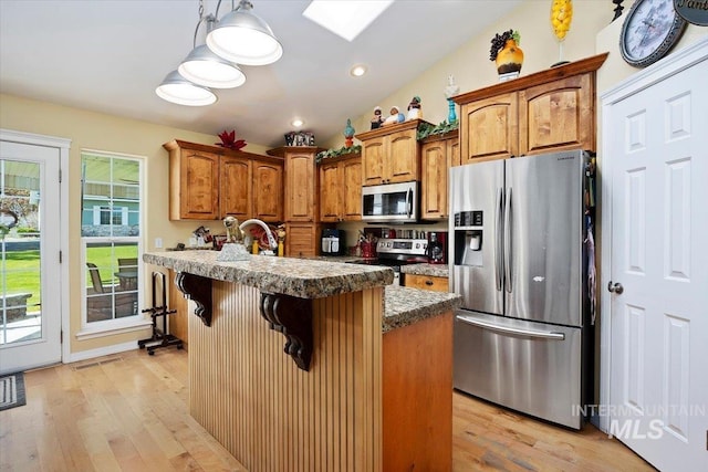 kitchen with a kitchen island, stainless steel appliances, light wood-type flooring, and lofted ceiling with skylight