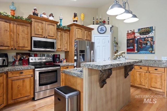 kitchen featuring stainless steel appliances, a center island, light hardwood / wood-style flooring, and decorative light fixtures