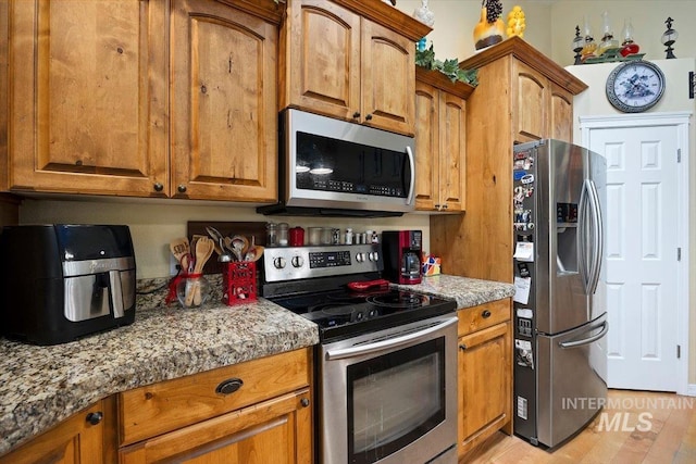 kitchen with stone countertops, appliances with stainless steel finishes, and light wood-type flooring