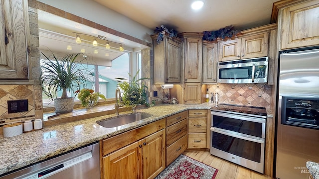 kitchen with tasteful backsplash, appliances with stainless steel finishes, light stone countertops, light wood-style floors, and a sink