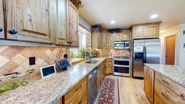 kitchen featuring light stone counters, stainless steel appliances, decorative backsplash, a sink, and light wood-type flooring