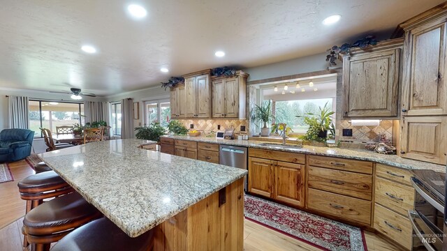 kitchen with decorative backsplash, a breakfast bar, a center island, light stone countertops, and a sink