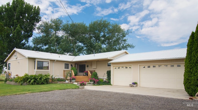 ranch-style home with driveway, metal roof, an attached garage, a front lawn, and stucco siding