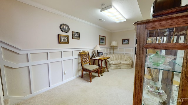 sitting room featuring crown molding, a decorative wall, visible vents, and light colored carpet