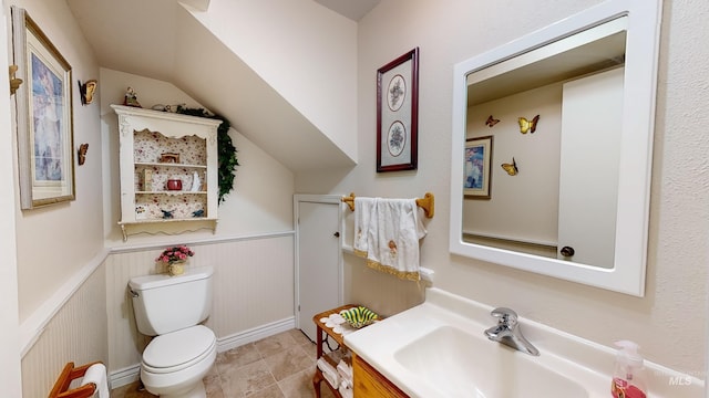 bathroom featuring lofted ceiling, wainscoting, vanity, and toilet