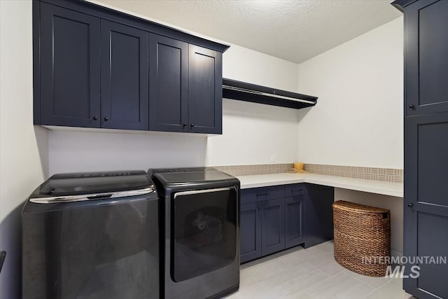 laundry room featuring cabinets, light tile patterned floors, a textured ceiling, and separate washer and dryer