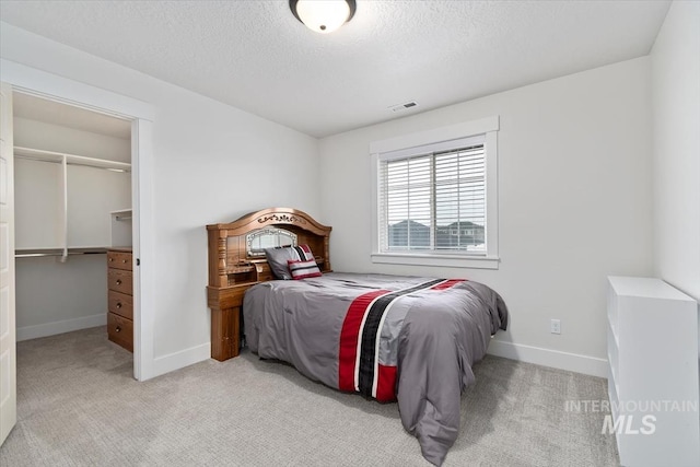 carpeted bedroom with a walk in closet, a textured ceiling, and a closet