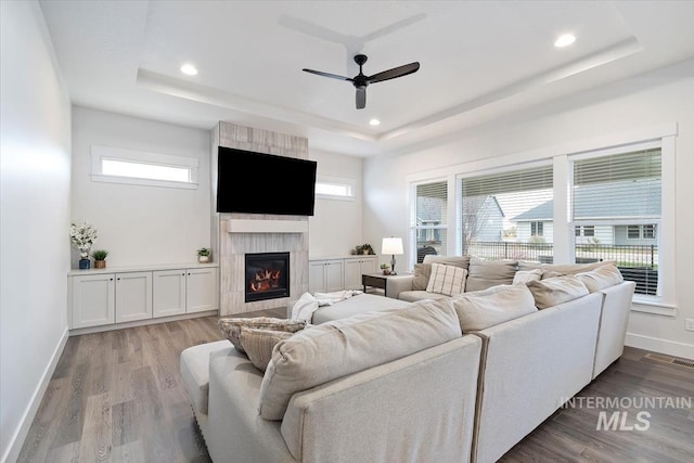 living room with a tray ceiling, a tile fireplace, ceiling fan, and light hardwood / wood-style floors