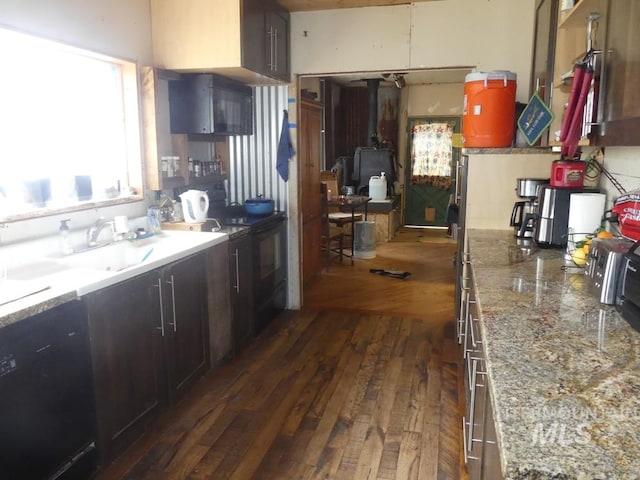 kitchen featuring a wood stove, dark brown cabinets, dark wood-type flooring, and black dishwasher