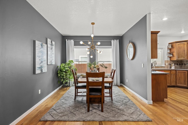 dining area with an inviting chandelier, sink, light hardwood / wood-style flooring, and a textured ceiling