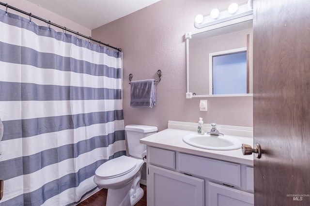 bathroom with vanity, curtained shower, toilet, and a textured wall