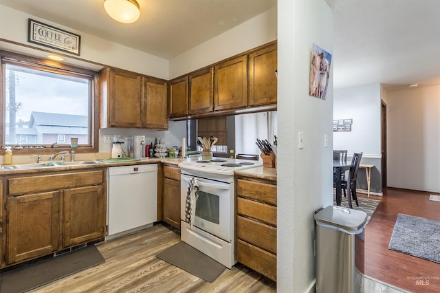 kitchen featuring white appliances, brown cabinets, light wood finished floors, and a sink