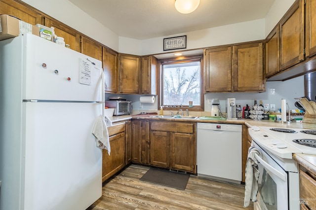 kitchen with light countertops, light wood-style flooring, brown cabinets, white appliances, and a sink