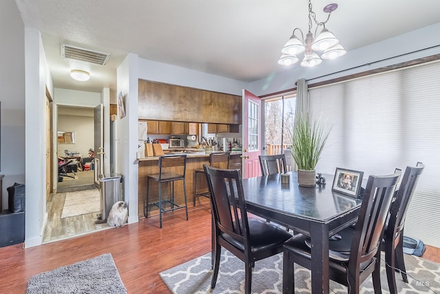 dining area with wood finished floors, visible vents, and a chandelier