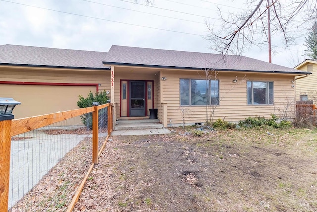 ranch-style house with an attached garage, a shingled roof, and fence