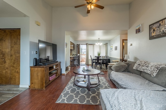 living room with ceiling fan with notable chandelier, a high ceiling, baseboards, and dark wood-style flooring