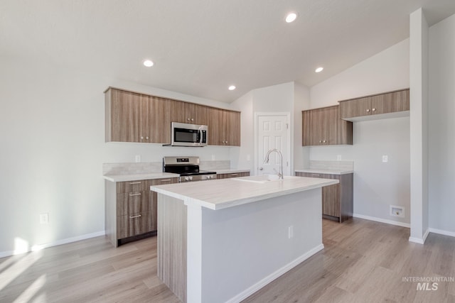 kitchen with appliances with stainless steel finishes, vaulted ceiling, sink, light wood-type flooring, and a center island with sink