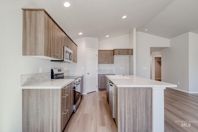 kitchen featuring vaulted ceiling, sink, light hardwood / wood-style flooring, an island with sink, and stainless steel appliances